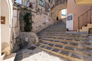 A set of stone steps leading up to a building entrance, with a small shrine at the bottom and a mural on the wall.