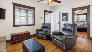 A spacious room with a ceiling fan, two leather recliners, a wooden chest of drawers, and a large window with blinds. - Historic 1919 Home | Walk to Downtown (Prescott)