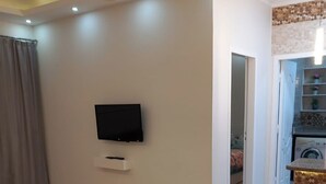 A living room with a flat-screen TV mounted on the wall, a small cabinet below it, and a patterned rug on the floor. - 1 bedroom apartment sleeping 2 people's only (Sharm Elshake)