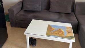 Una sala de estar con una mesa de centro blanca, un sofá gris y un par de pantuflas negras en el suelo.