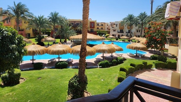 Un resort con varias piscinas, palmeras y sombrillas de paja.