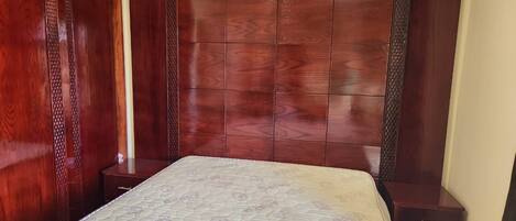 Un dormitorio con cabecera de madera, colchón, mesita de noche y aire acondicionado instalado en la pared.