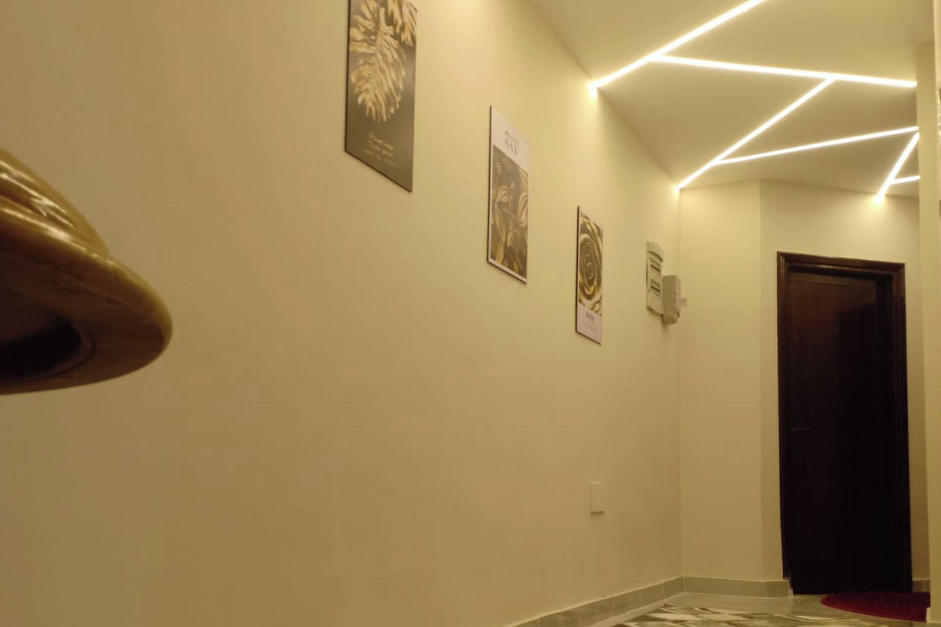 A hallway with a wooden handrail, a tiled floor, and wall-mounted light fixtures.