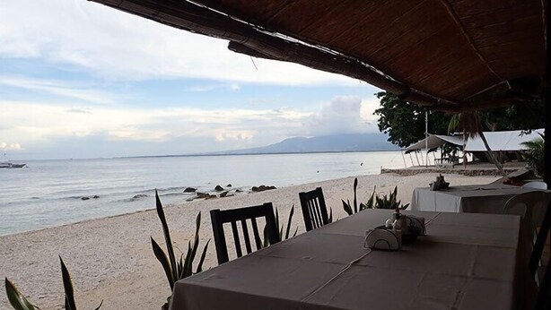 A beachside dining area with a table set for two, overlooking the sea. - Lubi Resort (Santander)