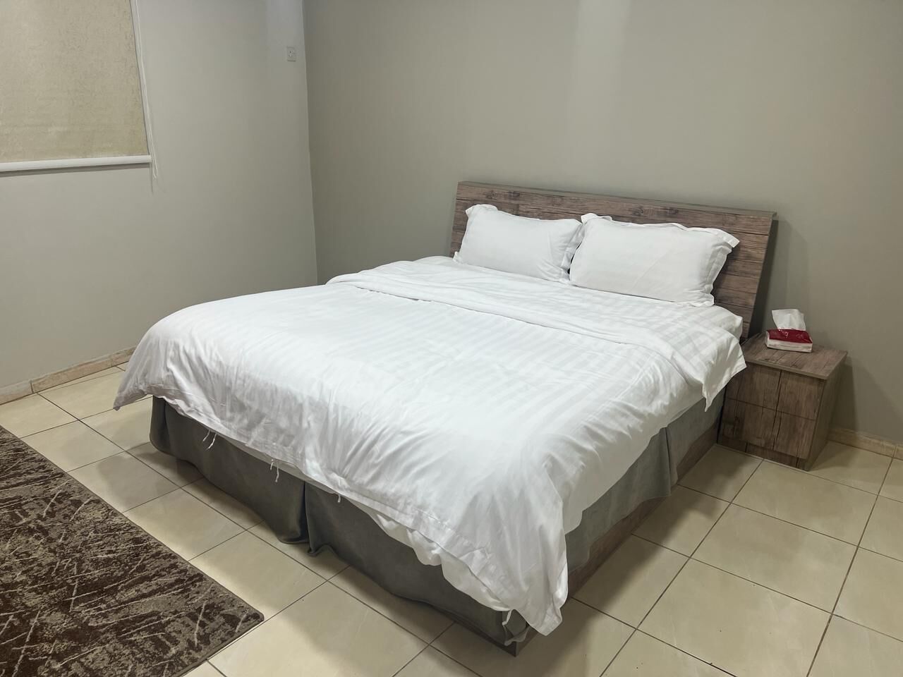 A neatly made bed with white linens, a wooden headboard, and a small bedside table with a tissue box.