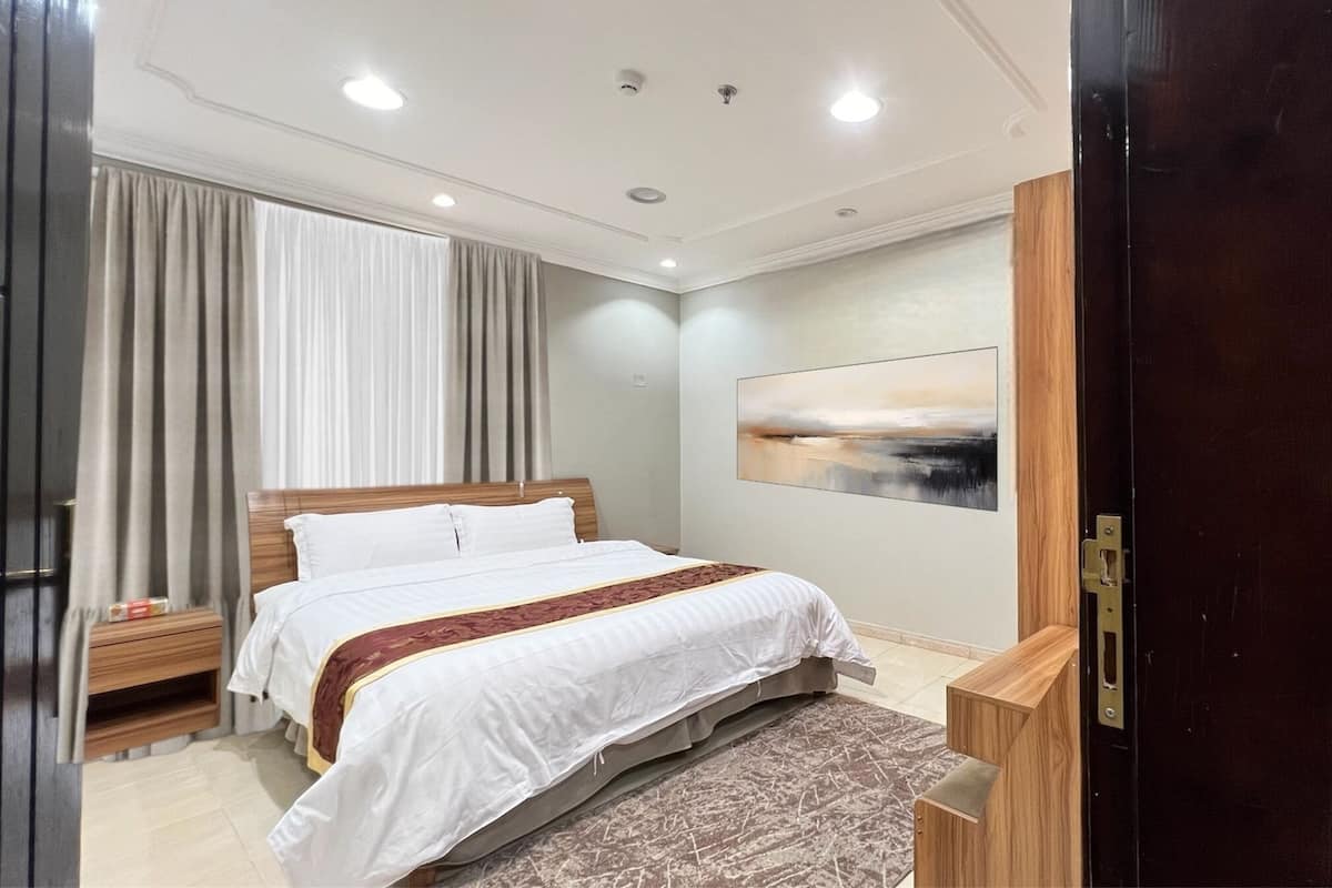 A modern hotel room with a large bed, a wooden nightstand, a desk, and a painting on the wall.