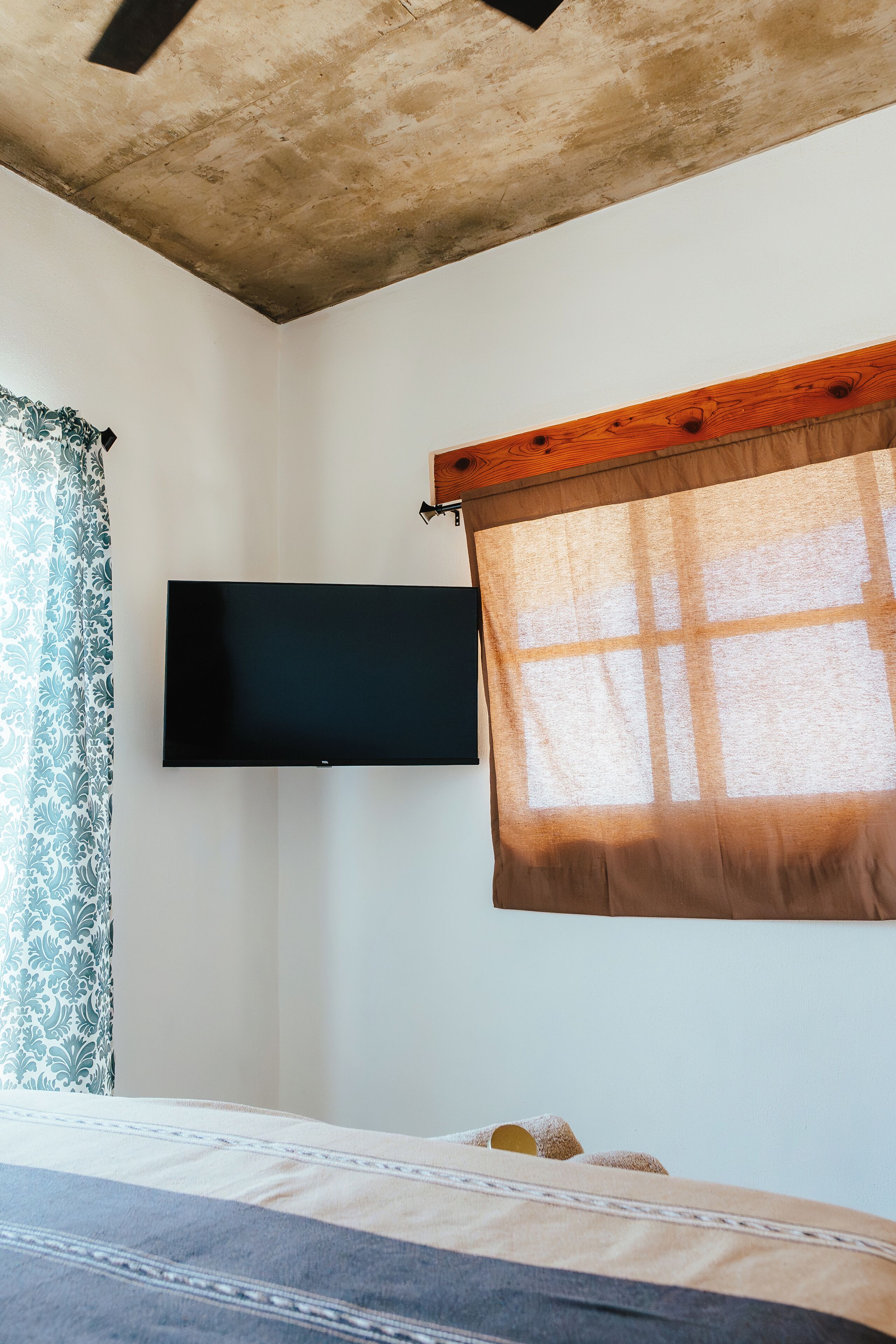Ein Schlafzimmer mit Bett, einem flachbildfernseher an der Wand und einem Fenster mit Vorhang.