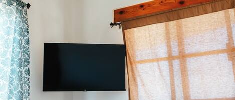 Une chambre à coucher avec un lit, un téléviseur à écran plat fixé au mur et une fenêtre avec un rideau.