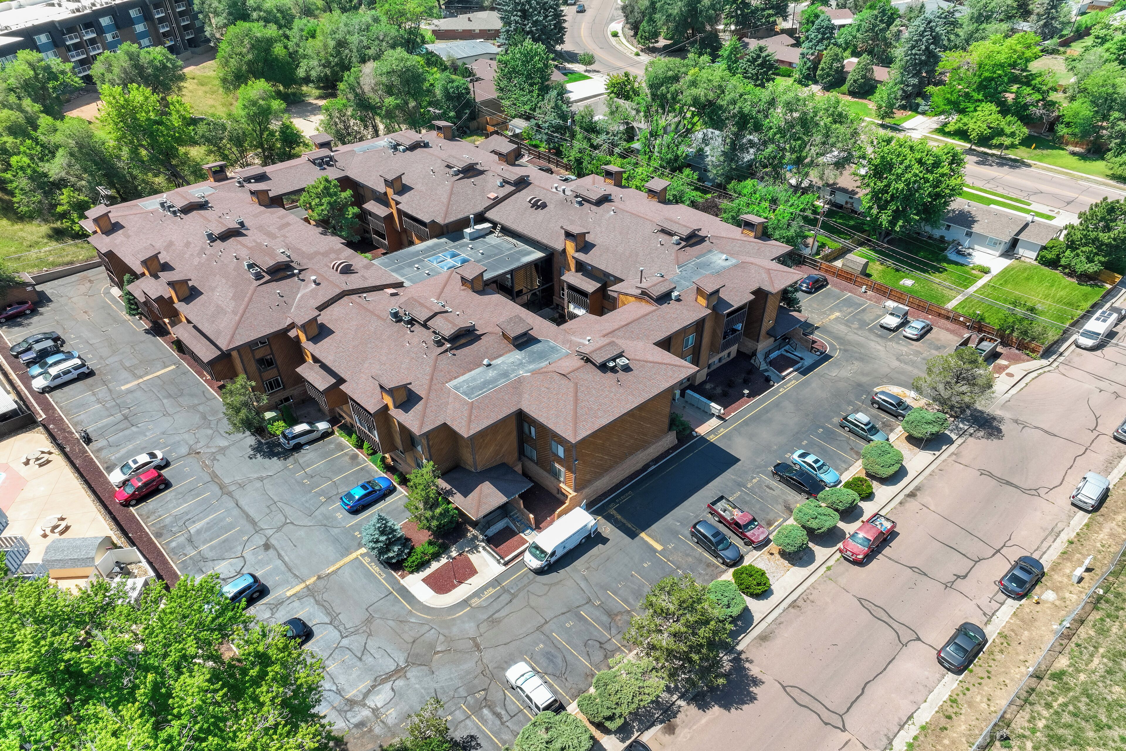 A multi-story building with a parking lot, surrounded by trees and a road.