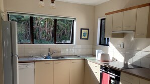 A modern kitchen with a dishwasher, sink, and stove. There is a window with a view of greenery outside.
