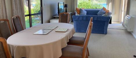 Une pièce comprenant une table à manger, des chaises, un canapé et offrant une vue sur la verdure et les montagnes grâce à de grandes fenêtres.