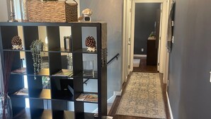 Un couloir doté d’un parquet en bois foncé, d’une étagère noire ornée d’objets décoratifs et d’un tapis à motifs.