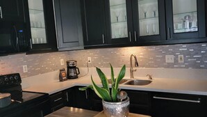 Une cuisine moderne avec des meubles de couleur sombre, un plan de travail blanc, un évier et une cuisinière.
