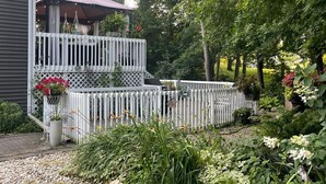 Une terrasse à deux niveaux, agrémentée d’une pergola, entourée d’une clôture en bois peinte en blanc, et un jardin avec des galets et des plantes.