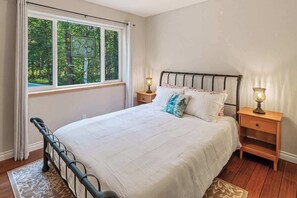Une chambre à coucher avec un lit, deux tables de chevet, une fenêtre donnant sur des arbres et un tapis à motifs.