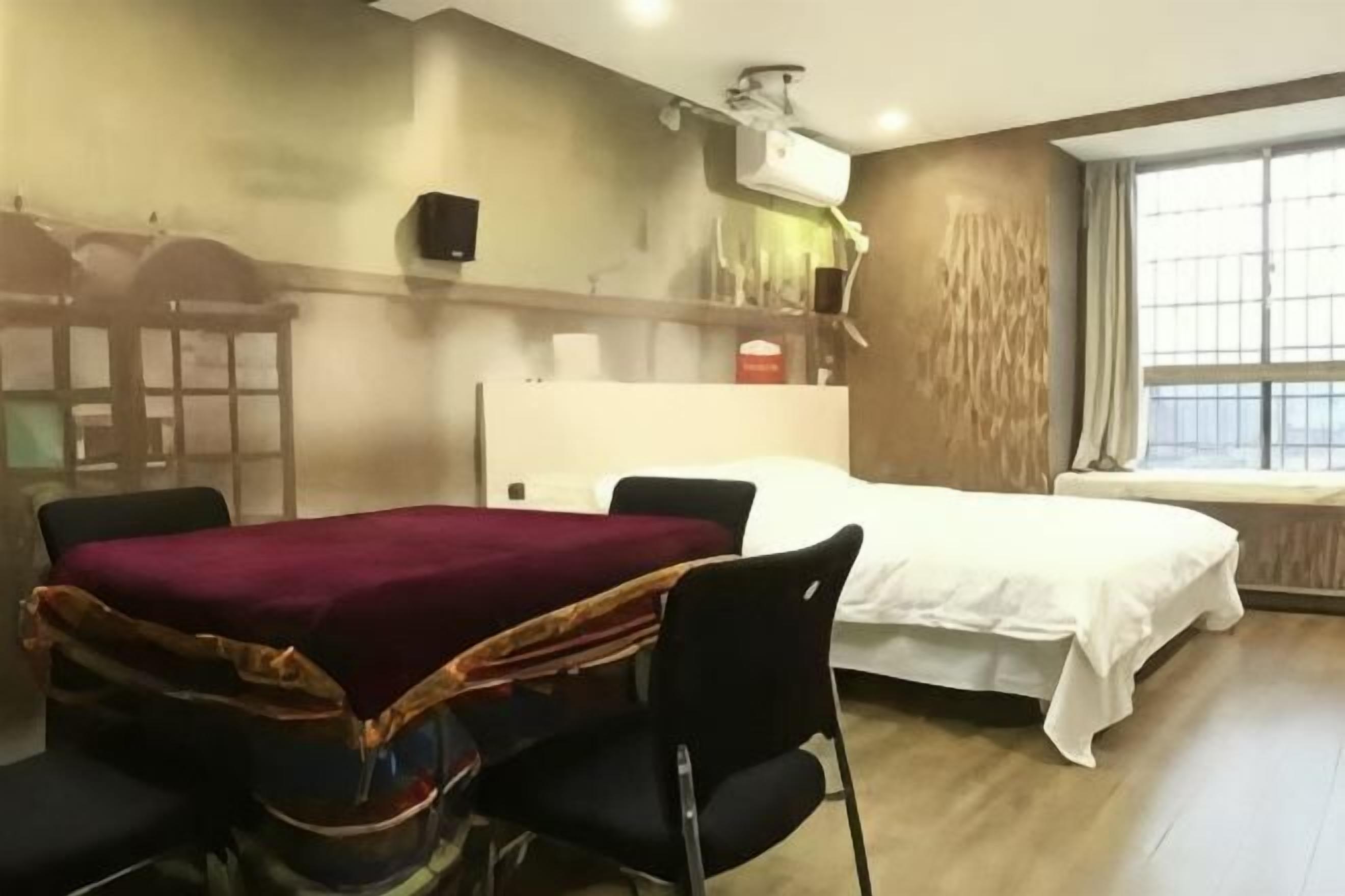 Hotelkamer met een bed, een bureau met stoel, een raam en een luchtverkoeler aan de wand.