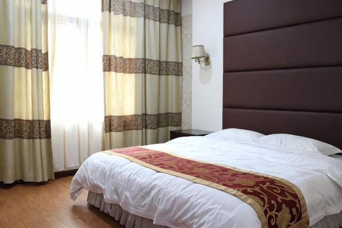 Une chambre dâhĂŽtel avec un grand lit, des rideaux, une lampe fixĂ©e au mur et un plancher en bois.