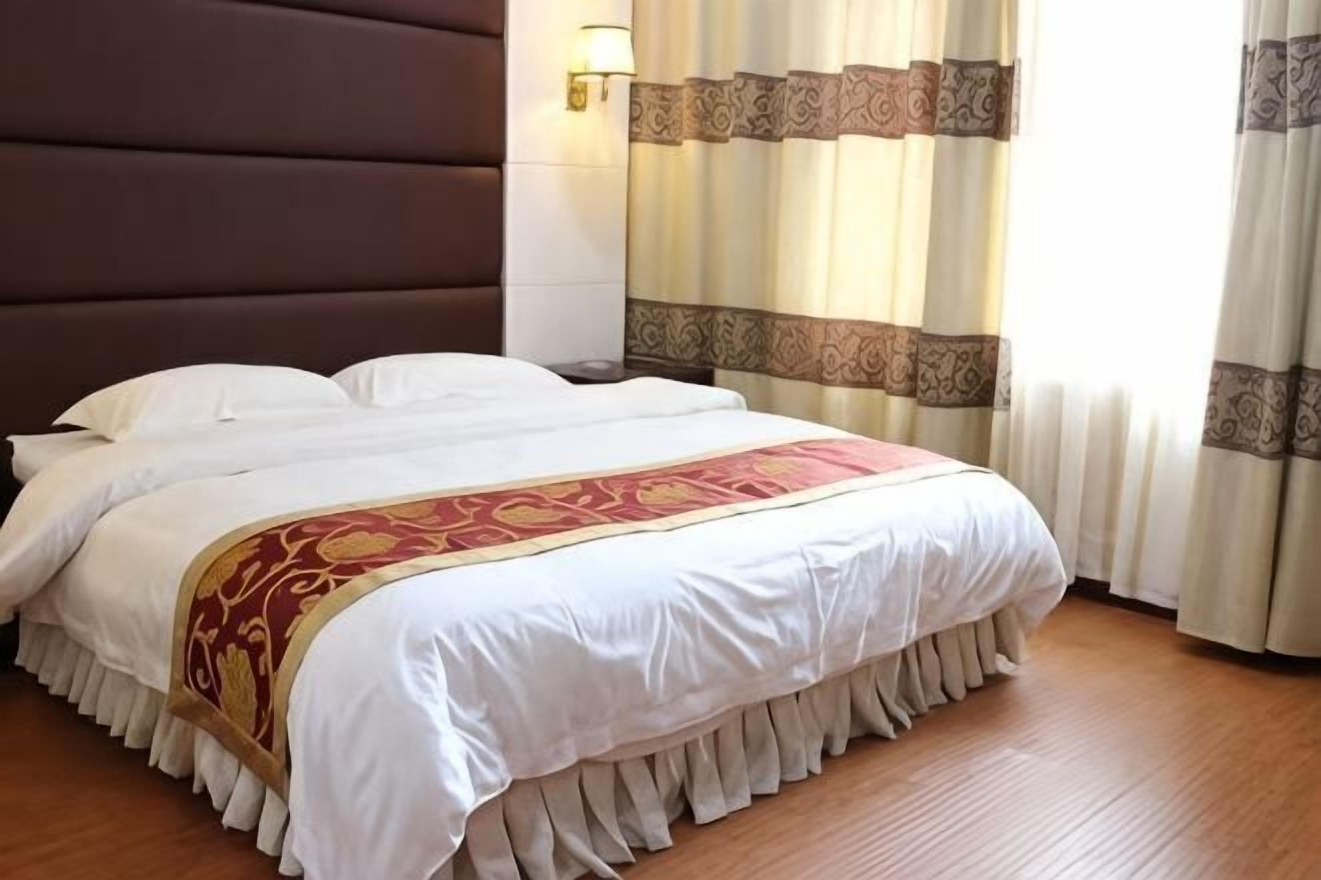 Een hotelkamer met een groot bed, hoofdeinde, gordijnen en een wandlamp.