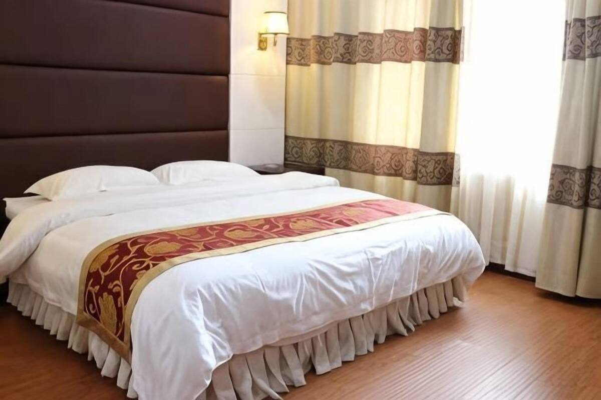 Une chambre dâhĂŽtel avec un grand lit, une tĂȘte de lit, des rideaux et un luminaire fixĂ© au mur.