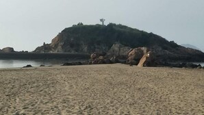 A beach with a rocky outcrop and a statue on top. - Shengsi Yajing Homestay (Shengsi)