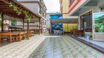 A covered outdoor seating area with tables and chairs, a tiled floor, and a building with a colorful facade.