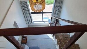 A staircase with a wooden handrail, a hanging wicker light fixture, and a view of the outdoors through a window with curtains. - Duplex Vista Lagoa by La Playa (Ipojuca)