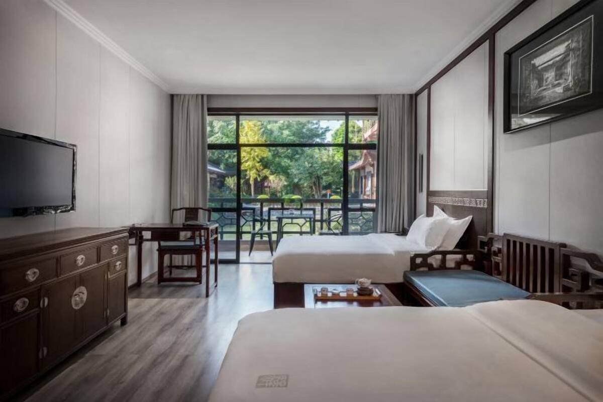A hotel room with two beds, a TV, a wooden dresser, and a balcony with outdoor furniture.