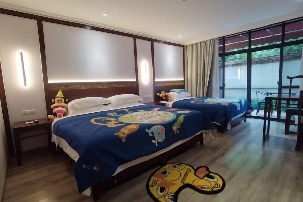 A hotel room with two beds, a desk, and a large window.