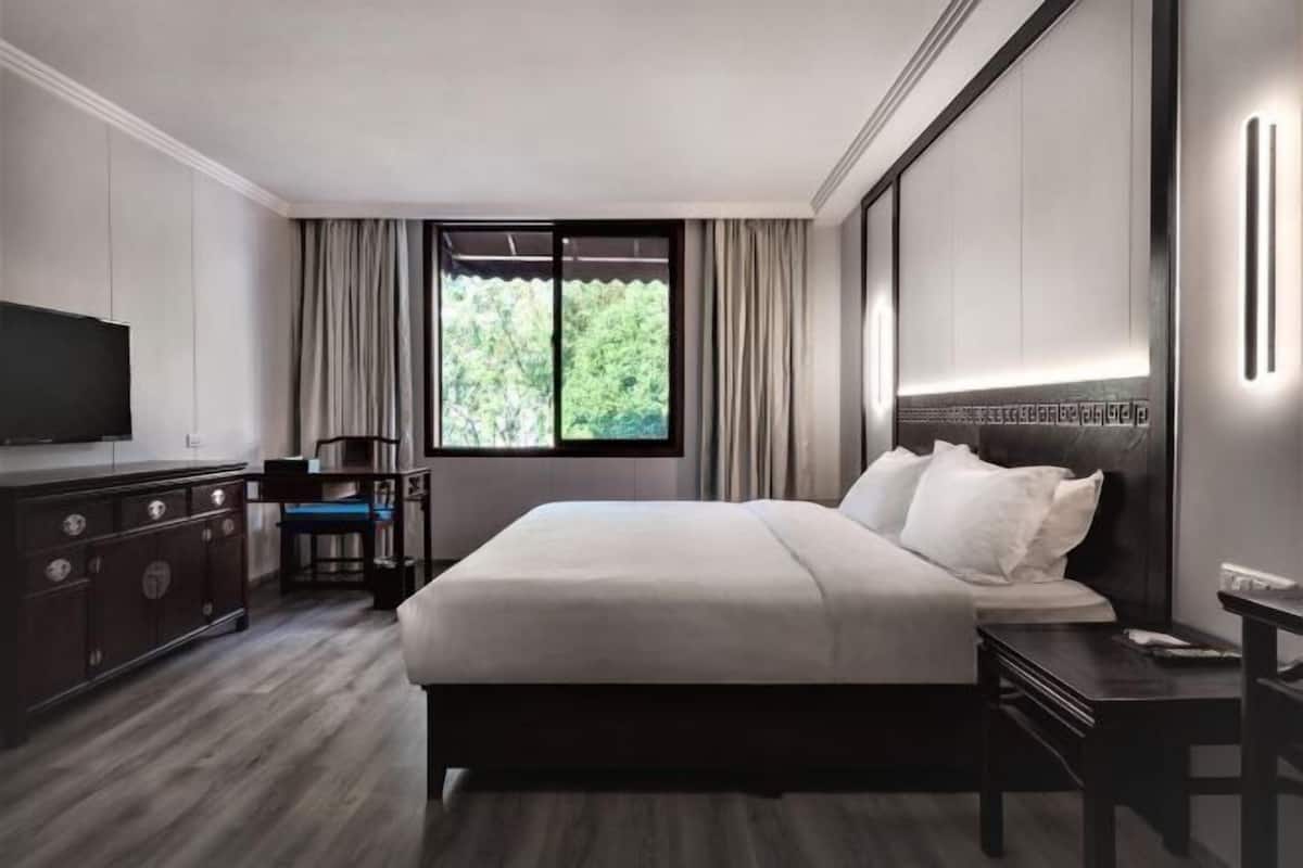 A modern hotel room with a large bed, a TV, a desk, and a window with curtains.