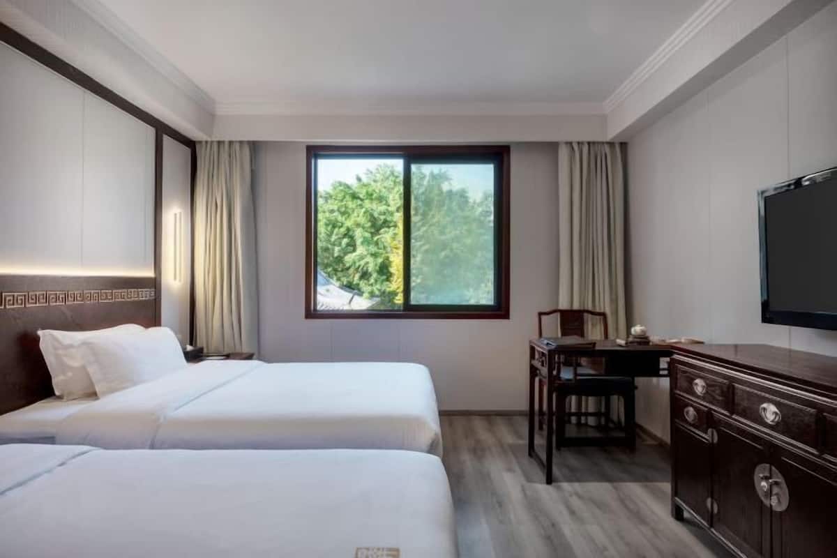 A hotel room with two beds, a desk, a dresser, and a TV.