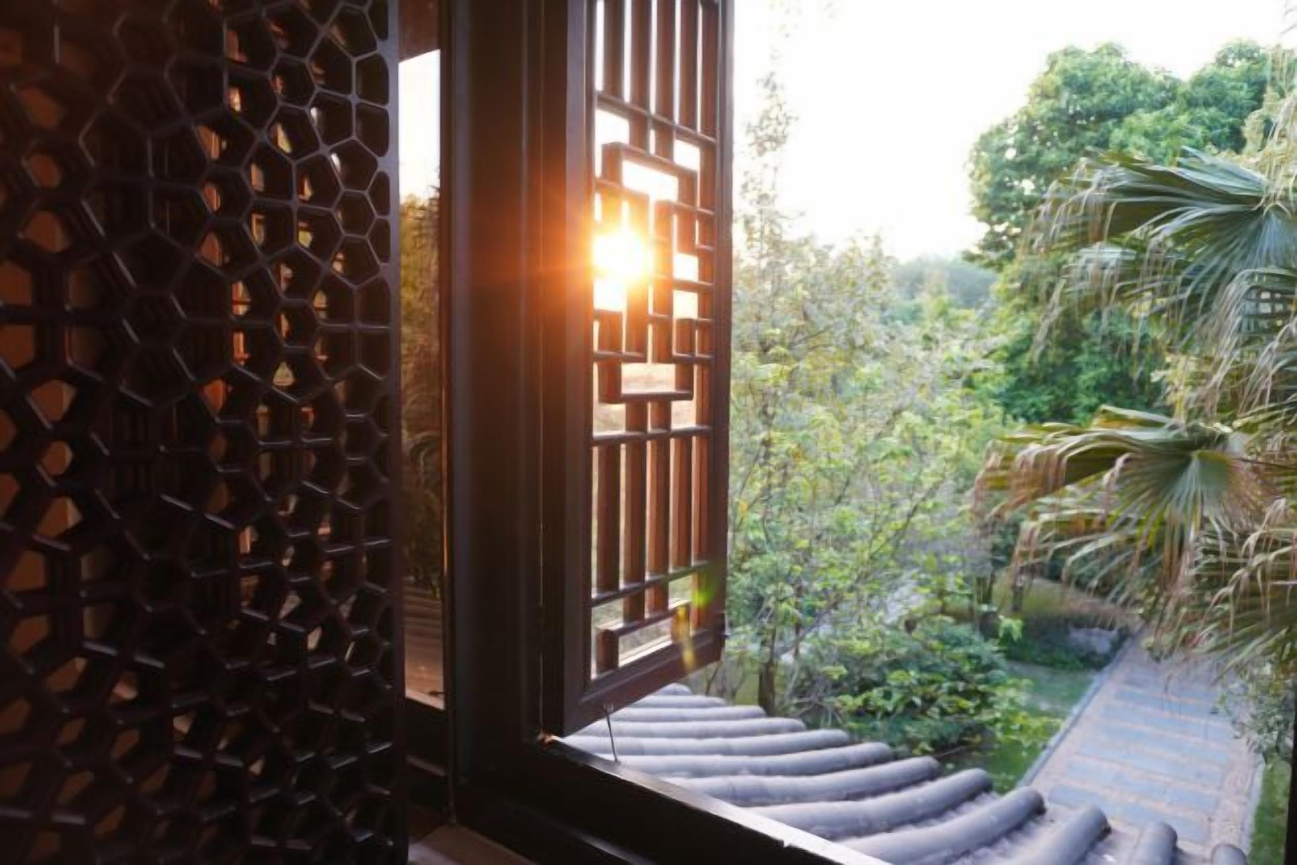 Una ventana con un diseño geométrico, vista a un jardín con árboles y una escalera que lleva a una azotea.