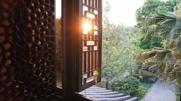 Una ventana con un diseño geométrico, vista a un jardín con árboles y una escalera que lleva a una azotea.