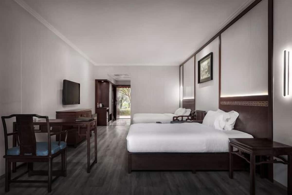 A hotel room with a bed, a desk, a chair, a television, and a framed picture on the wall.