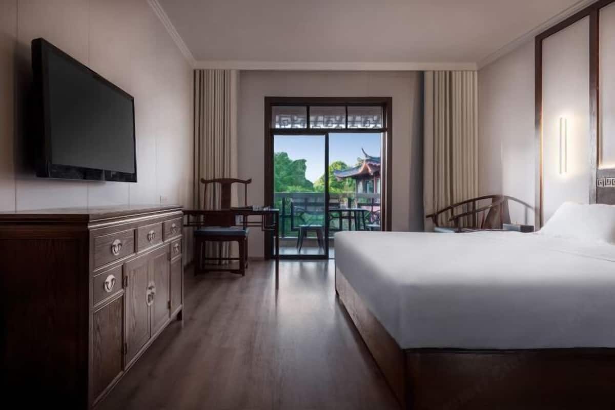 A hotel room with a bed, a TV, a desk, and a balcony with a view.
