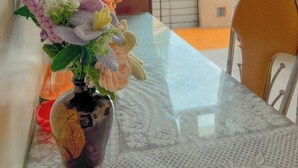 A dining table with a vase of flowers, a chair, and a view of buildings through a window with curtains. - HOA LAN HOTEL (Xuan Huong - Da Lat)