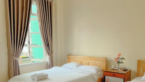 A hotel room with two beds, a small bedside table with a phone and a vase of flowers, and a window with curtains. - HOA LAN HOTEL (Xuan Huong - Da Lat)