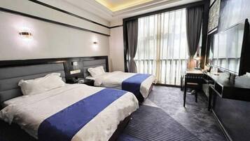 A hotel room with two beds, a desk, a chair, a TV, and a large window with curtains.