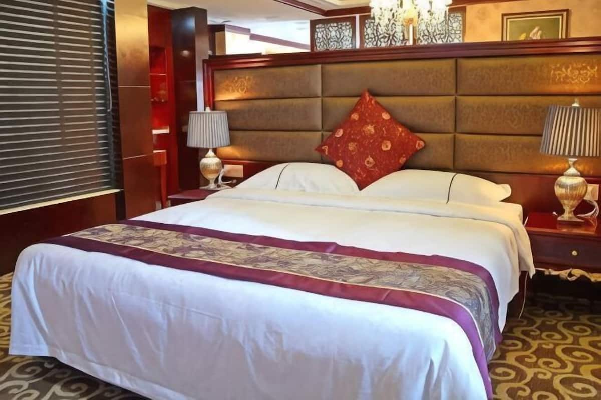 A hotel room with a large bed, two bedside tables, a headboard, and a patterned carpet.