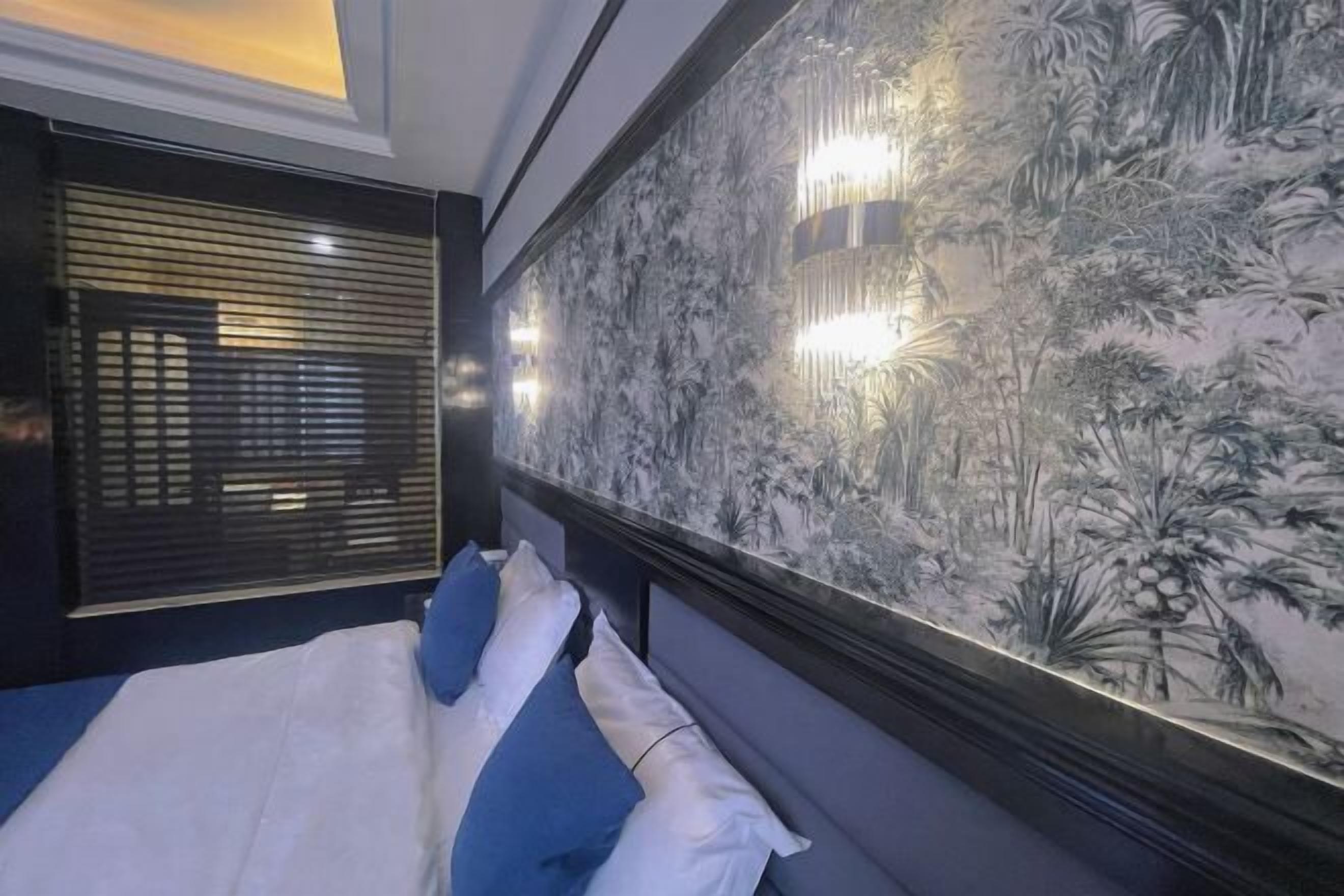 A bedroom with a bed, a wall with a nature-themed mural, and a window with blinds.