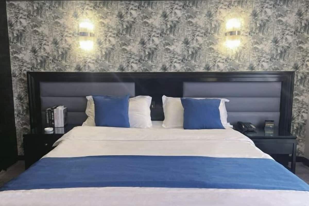 A bed with a headboard, two bedside tables, and wall-mounted lights.