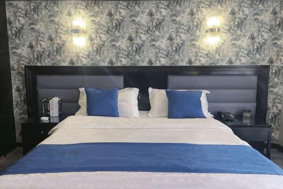A bed with a headboard, two bedside tables, and a wall with a patterned wallpaper.