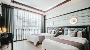 Ein Hotelzimmer mit zwei Betten, einem Schreibtisch und einem großen Fenster mit Vorhängen.
