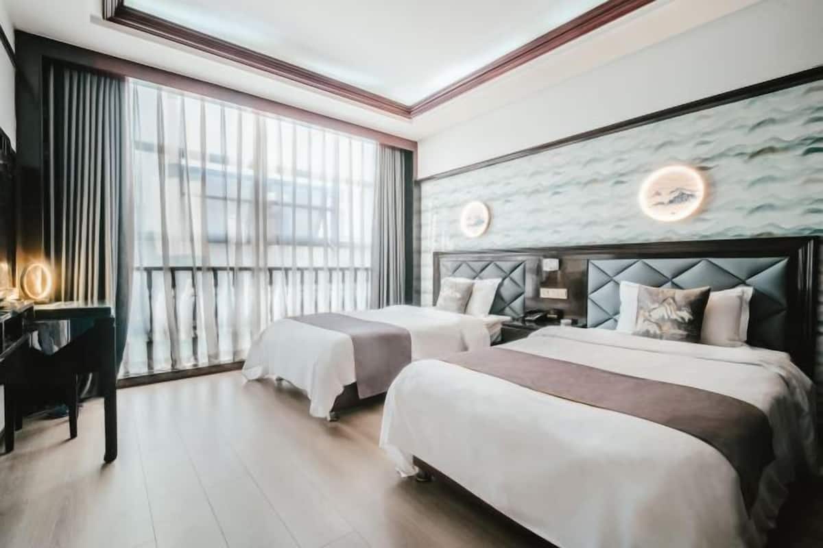 A hotel room with two beds, a desk, and a large window with curtains.