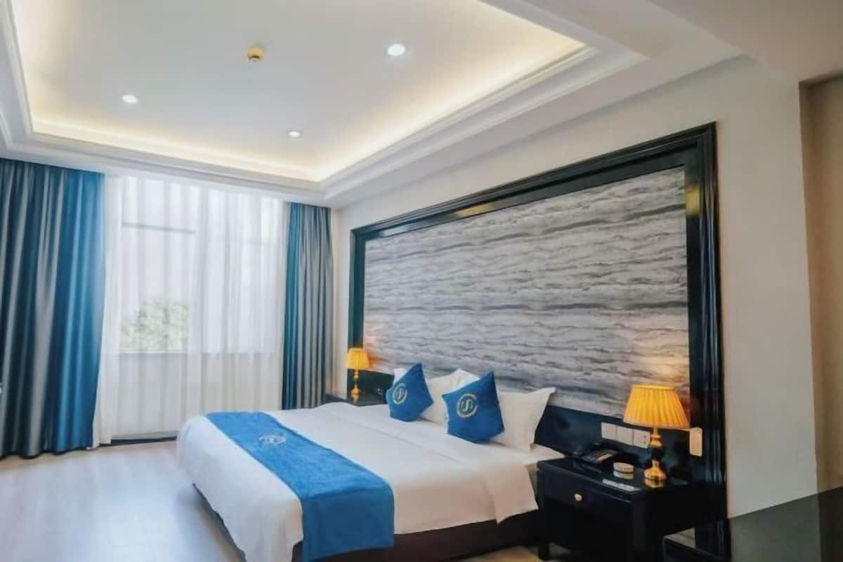 A modern hotel room with a large bed, a marble accent wall, and a nightstand with a lamp.