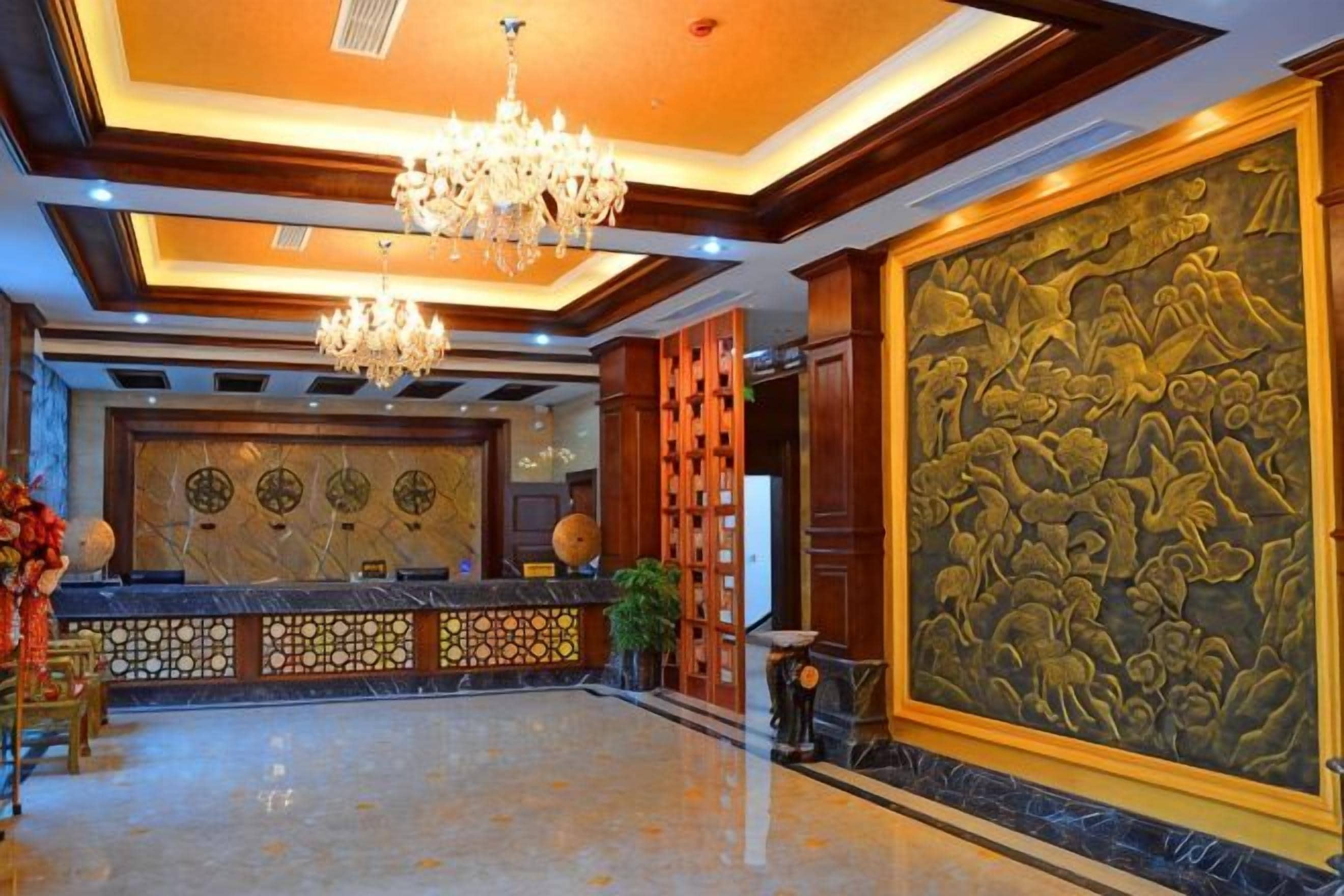 A lobby with a reception desk, chandeliers, and a large decorative wall.