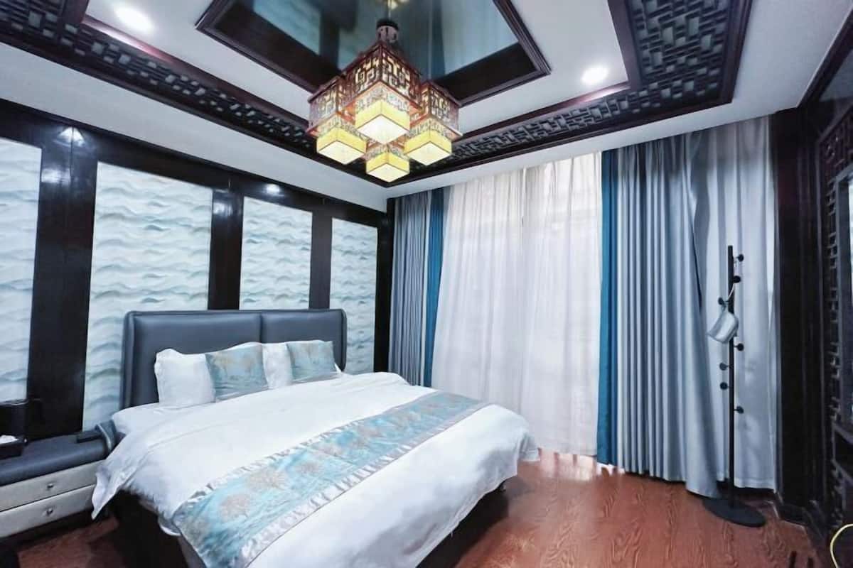 A bedroom with a large bed, a chandelier, and a view of the outside through the window.
