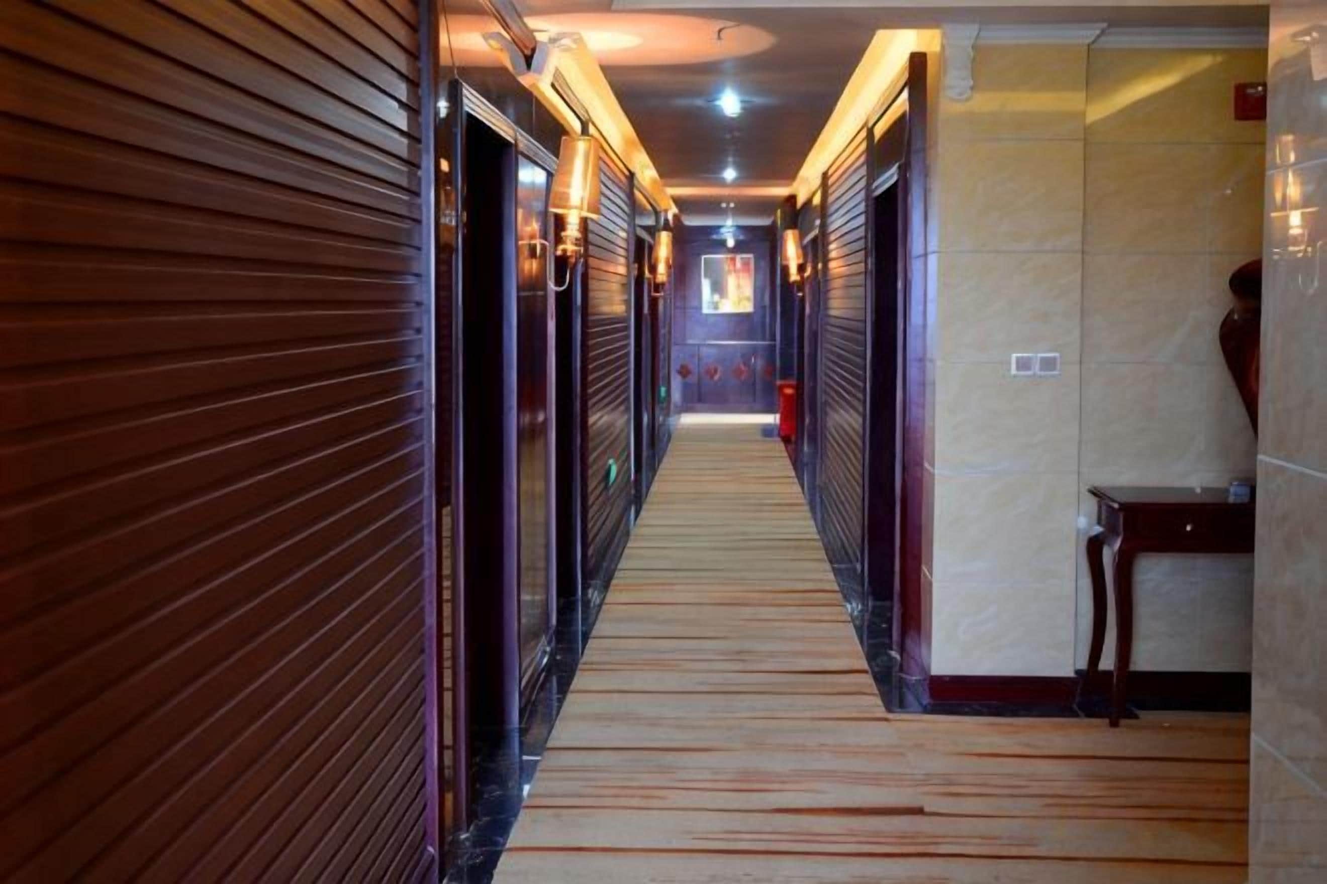 A corridor with closed doors, a wooden floor, and a tiled wall.