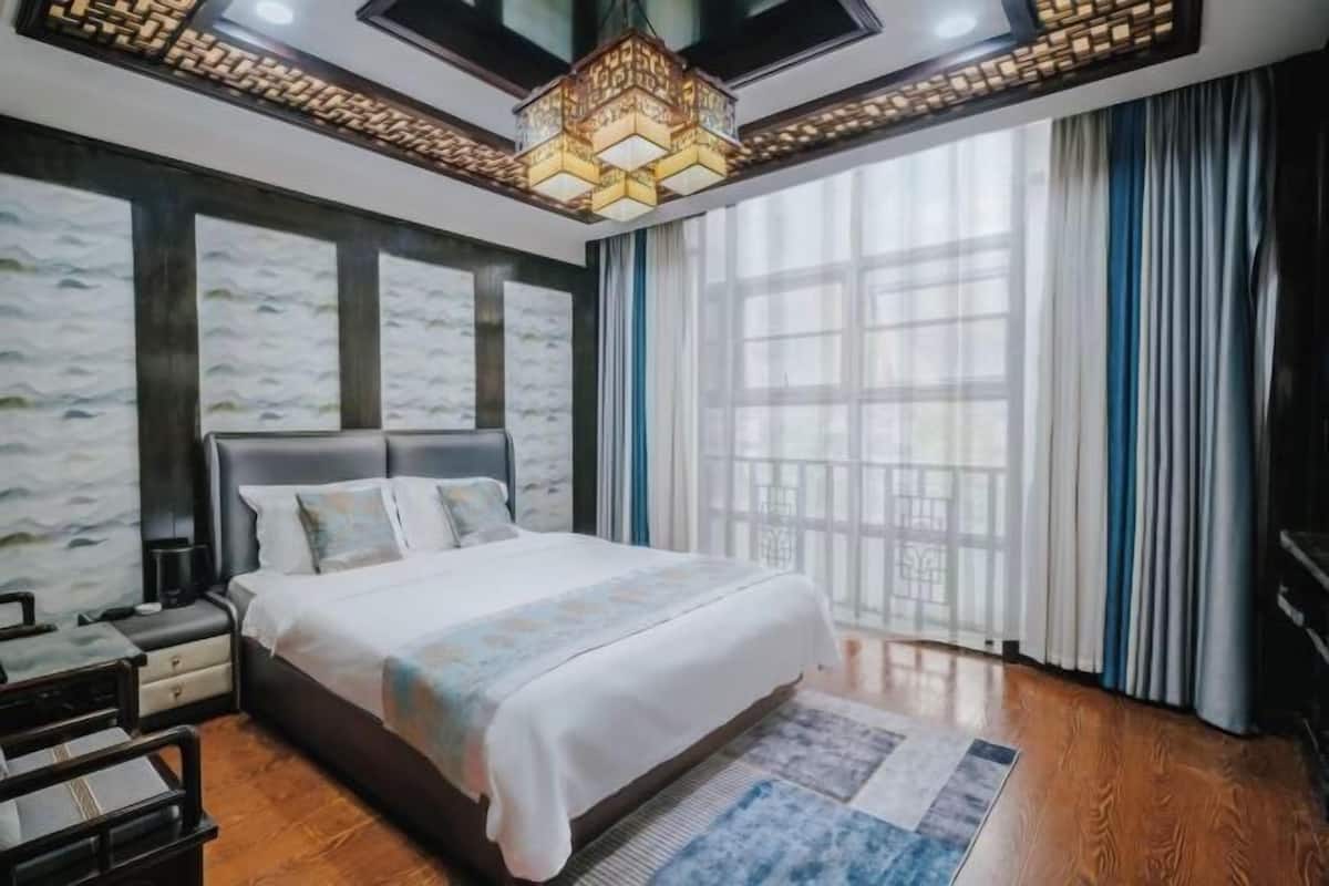 A bedroom with a large bed, a nightstand, a desk, and a window with curtains.