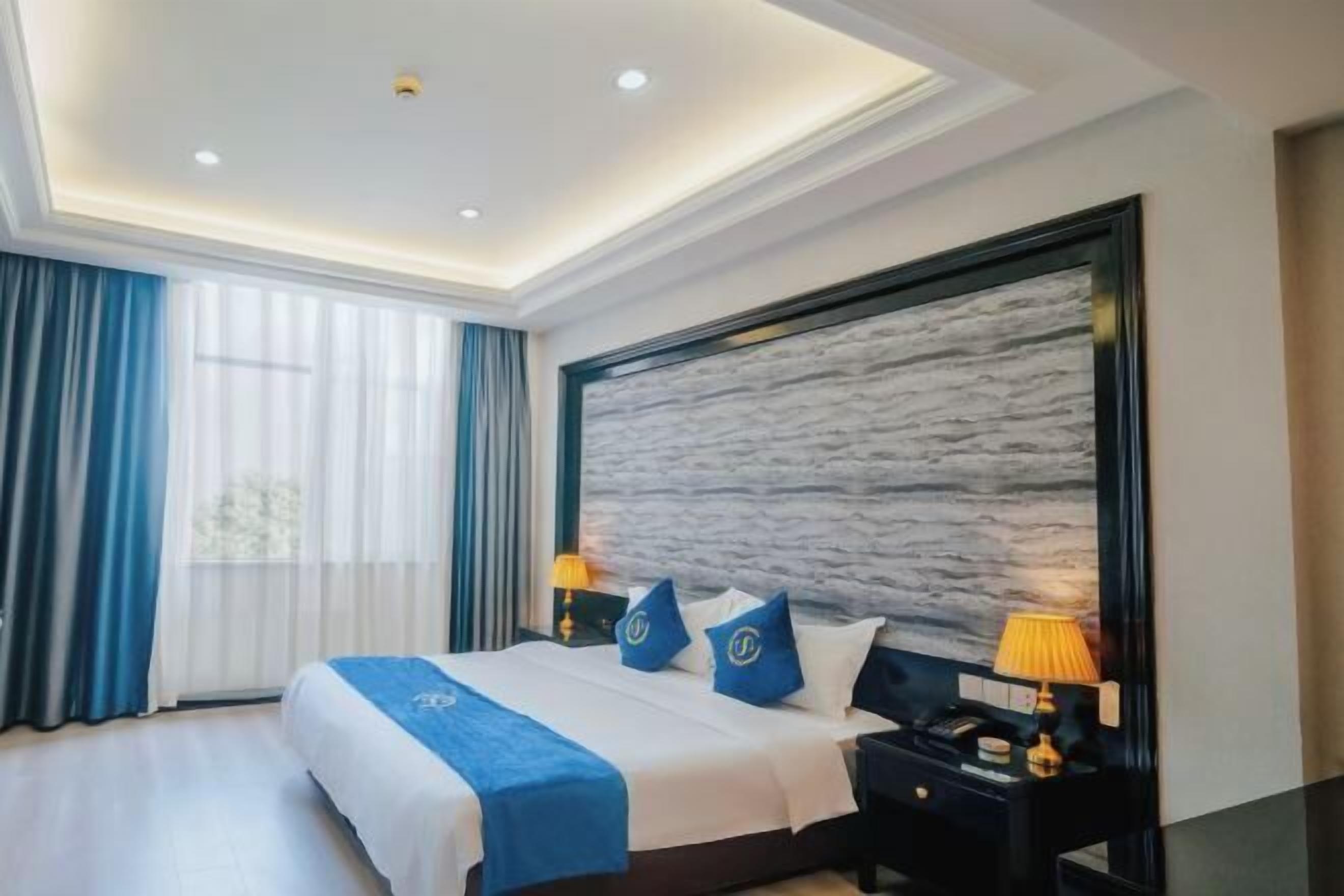 A modern hotel room with a large bed, two bedside tables, a nightstand, and a wall-mounted TV.