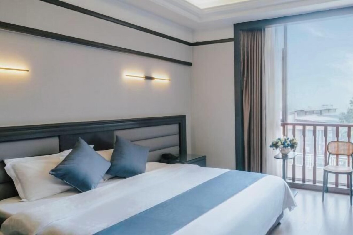 Ein Hotelzimmer mit einem Bett, einem Nachttisch, einem Fenster mit Vorhängen und einem Balkon mit Stuhl und Tisch.